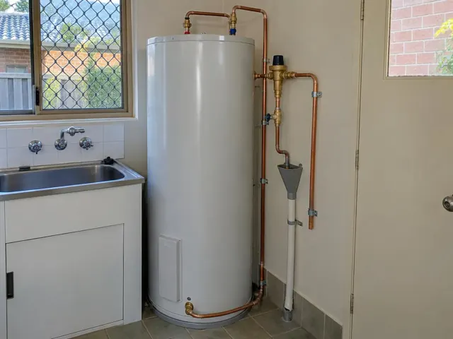 New hot water cylinder beside a laundry sink with copper pipework and tiled walls in Raymond Terrace