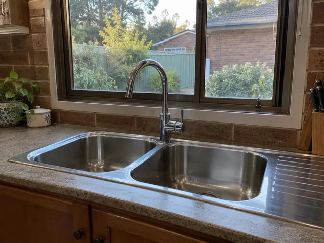 Stainless steel kitchen sink with a chrome mixer tap below a window in a brick home in Ferodale