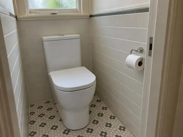 White toilet in a small tiled bathroom with patterned floor and frosted window in Raymond Terrace